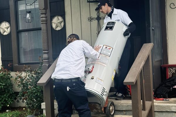 Two Of Underwood’s Trusted Plumbers Carrying A New Water Heater Into A Home.