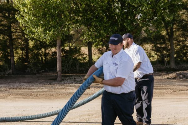 Two Of Underwood Plumbing’s Expert Technicians Carrying A Hose For Septic Maintenance.