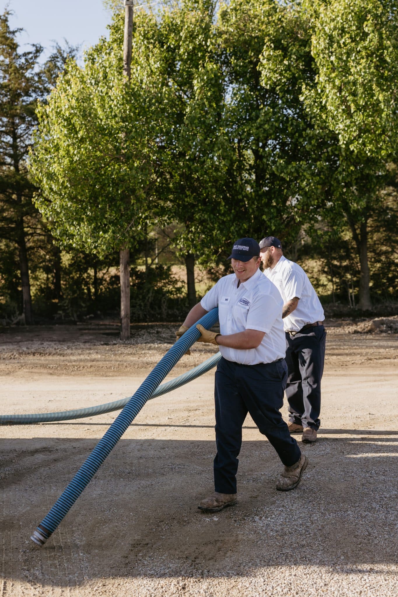 Two of Underwood Plumbing’s expert technicians carrying a hose for septic maintenance.