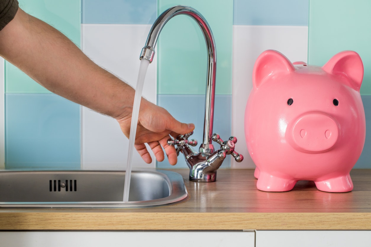 A person turning on their faucet next to a piggy bank representing high water bills.